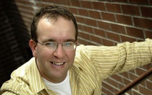Carl Ellswort posing by wearing white vest and yellow shirt.